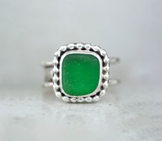 "Handcrafted Sterling Silver Statement Ring with Green Sea Glass. This chunky ring has been handmade using 925 Sterling Silver that has been fused, stamped and lightly oxidized. The setting is a shard of genuine Green Sea Glass that is in a Bezel setting accented with Bead Wire. The band is 1/4\" wide and the setting is 1/2\" wide and cannot be resized. Size 5 Add a touch of oceanic elegance to your everyday with this stunning Green Sea Glass Sterling Silver Statement Ring. Handcrafted with care, this ring showcases a vibrant, emerald-green sea glass gemstone that mirrors the captivating hues of the sea. The organic shape of the sea glass is beautifully complemented by the intricate sterling silver setting, adding a touch of whimsy and sophistication. With its bold and eye-catching design, Handmade Green Rings With Recycled Glass, Chunky Silver Rings, Sea Glass Ring, Beachglass Jewelry, Green Sea, Chunky Rings, Statement Ring Silver, Glass Rings, Beach Glass