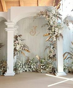 an archway decorated with white flowers and greenery in front of a wall that has gold lettering on it