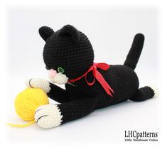 a crocheted black cat laying next to a ball of yarn