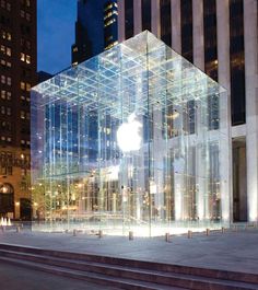 an apple store in the middle of a city at night with its glass facade lit up