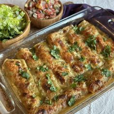 a casserole dish with meat, cheese and vegetables on the side next to a bowl of salad