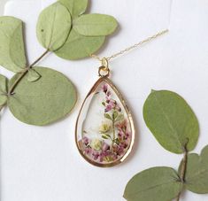 "A beautiful and unique Botanical inspired terrarium necklace with gorgeous real pressed Yorkshire Heather picked on the moors, gorgeous white and pink gypsophila and folliage.   Beautiful lilac flowers in a teardrop pendant.  For someone who needs to wish, for wishes to be granted and for communicating with the spirit world.  The flower is encapsulated in a crystal clear Resin which is Non-toxic, No VOCs, No fumes, No solvents, Non-flammable, Non-hazardous, No BPA.  The necklace chain is gold plated solid brass or stamped 14k gold filled chain as shown in last photo. This chain is much more long lasting and delicate.  The pendant is 1 inch in width and length.  A cute and eco friendly gift for yourself or a loved one. 🌼 So someone you love can bring spring with them wherever they go 🌼 Nature-inspired Gold Teardrop Pendant Jewelry, Unique Gold Keepsake Jewelry, Nature-inspired Rose Gold Necklace, Pink 14k Gold Filled Jewelry For Gift, Pink 14k Gold Filled Jewelry Gift, Handmade Yellow Gold Keepsake Jewelry, Nature-inspired Personalized Jewelry For Weddings, Personalized Nature-inspired Jewelry For Weddings, Personalized Nature-inspired Jewelry For Wedding