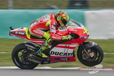 a man riding on the back of a red motorcycle down a race track with grass in the background