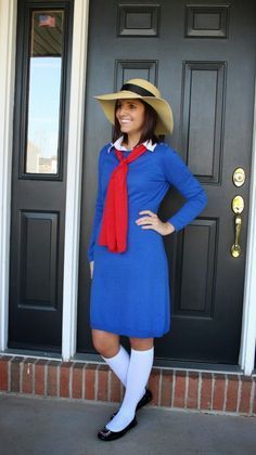 a woman standing in front of a door wearing a blue dress and hat with red scarf