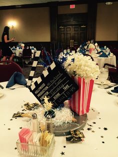 a table topped with popcorn buckets filled with flowers and confetti next to a chalkboard sign