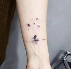 a woman's arm with a small tattoo on the wrist that has an image of a bird flying in space