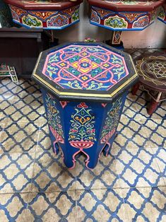 an ornately painted table sits in the middle of a room with other tables and stools