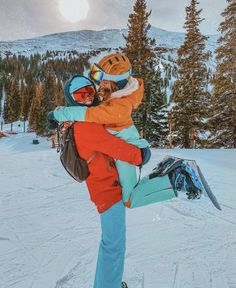 a man holding a woman on his back while standing in the snow with trees behind him