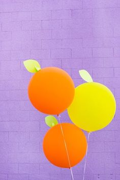 three balloons in front of a purple wall with leaves on them, one orange and the other yellow