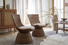 two wicker chairs sitting in front of a window next to a rug and table