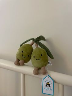 two green stuffed animals sitting on top of a white rail next to a tag that says jellycat