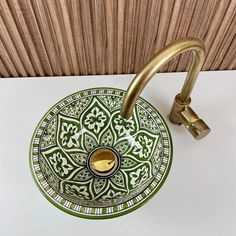 a green and white bowl with a brass faucet