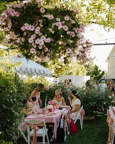 several women sitting at tables outside in the grass with pink and white flowers on them