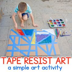 a young boy painting on the ground with tape resist art and paintbrushes next to him