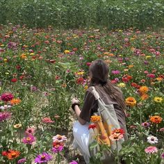 a woman kneeling down in a field full of wildflowers with her back to the camera