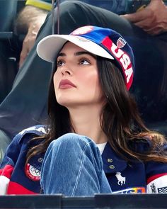 a woman sitting in the stands at a baseball game wearing a hat and blue jeans