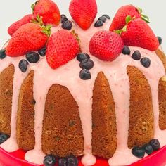 a bundt cake with strawberries and blueberries on top is sitting in a red bowl