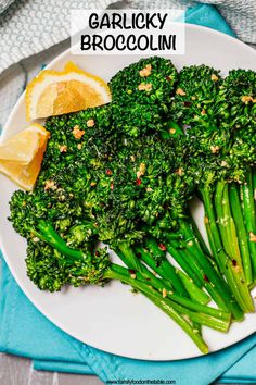 a white plate topped with broccoli covered in seasoning next to lemon wedges