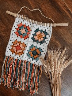 a crocheted wall hanging on a wooden floor next to some dried grass and straw stalks