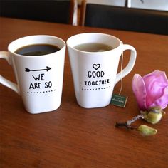 two coffee mugs sitting on top of a table next to a pink flower and a tag