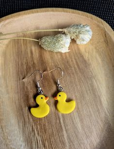 a pair of yellow rubber ducky earrings sitting on top of a wooden table next to dried flowers