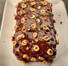 a piece of chocolate cake with nuts on top sitting on a white platter, ready to be eaten