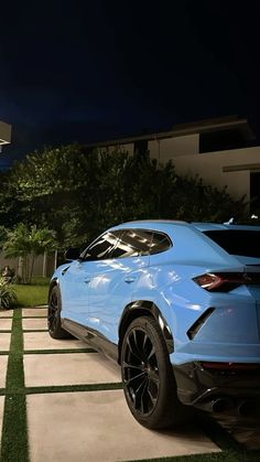 a blue sports car parked in front of a house at night with grass on the ground