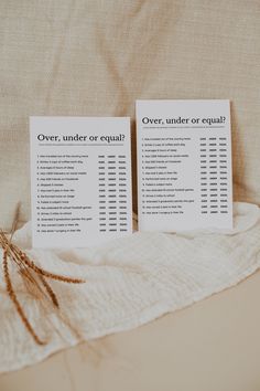 two paper signs sitting on top of a bed next to a white blanket and pillows