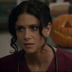 a woman with a stethoscope on her neck looking at the camera while standing in front of a pumpkin