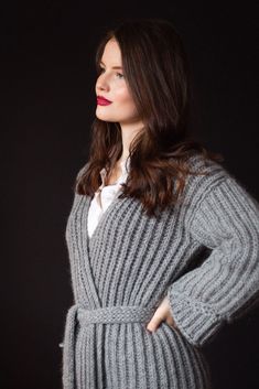 a woman standing in front of a black background wearing a gray sweater and white shirt