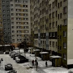 two people are walking in the snow near some buildings and parked cars on the street