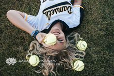 a woman laying on the ground with five softballs in her hand