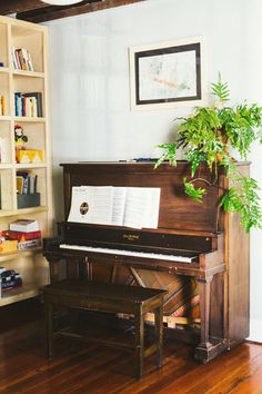 an old piano sits in front of a bookshelf filled with books and plants