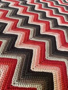 a crocheted blanket is laying on top of a bed with red, white and black stripes