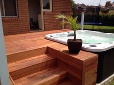 a hot tub sitting on top of a wooden deck next to a tree in a pot