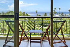 two wooden chairs sitting on top of a balcony next to an open door with the ocean in the background