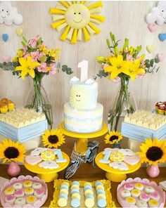 a table topped with lots of cakes and desserts next to sunflower covered walls