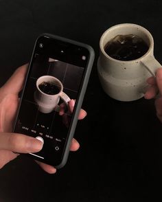 a person holding a cell phone next to a cup of coffee on a black table