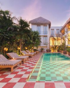 an outdoor swimming pool with chaise lounges and palm trees in the background at dusk