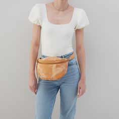 a woman in white shirt and jeans holding a tan fanny bag