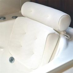 a white bath tub with two pillows on it's back and armrests