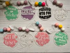 six key chains with different sayings hanging on a white wooden wall next to candy