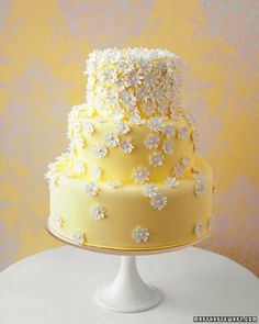 a three tiered yellow and white cake with flowers on the top is sitting on a table