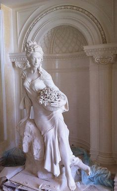 a statue of a woman sitting on top of a white chair with flowers in her hand