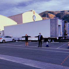 two people standing in the middle of a parking lot next to semis and trucks