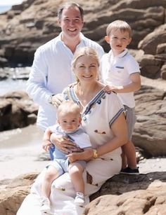 an older woman and two young boys are posing for a photo on the rocks by the water