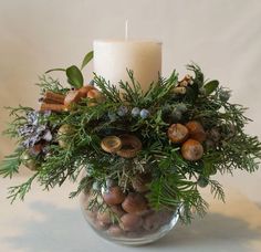 a candle that is on top of a glass vase filled with nuts and greenery