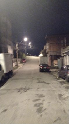 two trucks parked on the side of a road next to houses at night with street lights above them