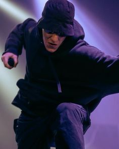 a man in black jacket and hat performing on stage with his arms out to the side