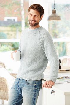 a man standing in the kitchen holding a coffee cup and smiling at the camera,